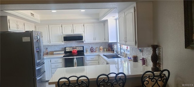 kitchen featuring a peninsula, a sink, white cabinetry, light countertops, and appliances with stainless steel finishes