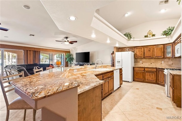 kitchen featuring open floor plan, vaulted ceiling, brown cabinets, white appliances, and a sink