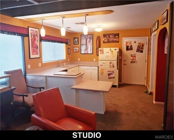 kitchen with light countertops, hanging light fixtures, freestanding refrigerator, white cabinetry, and a peninsula