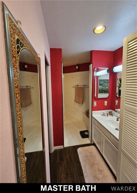 bathroom with a textured ceiling, wood finished floors, a shower stall, and vanity