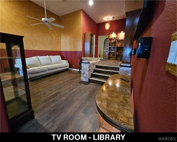 living room featuring baseboards, arched walkways, dark wood finished floors, and a ceiling fan