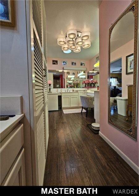 corridor featuring dark wood-style flooring, a notable chandelier, and baseboards