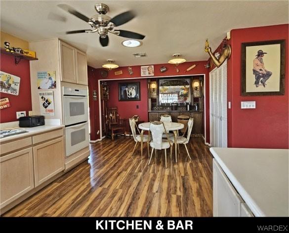 kitchen with light brown cabinets, light countertops, dark wood-style flooring, and white double oven