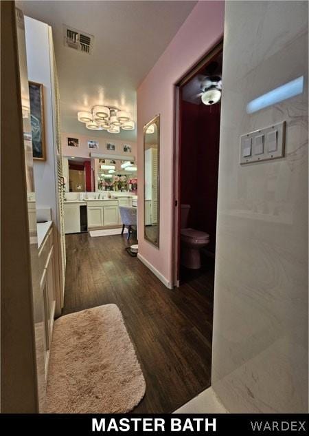 bathroom with toilet, vanity, wood finished floors, and visible vents