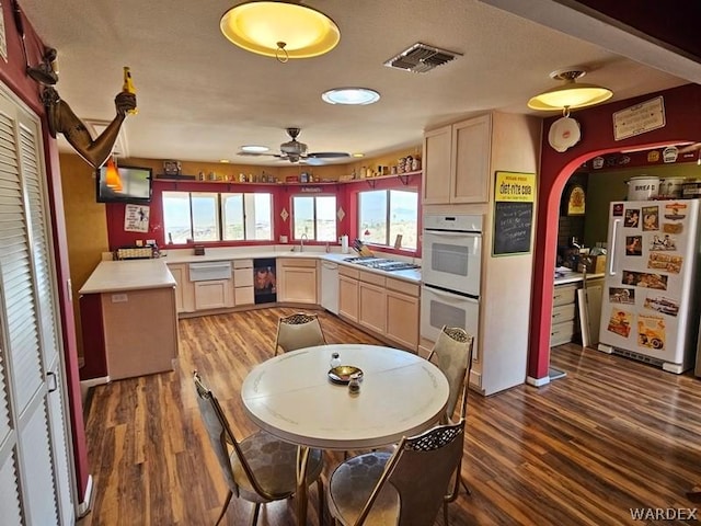 kitchen with dark wood-style floors, light countertops, visible vents, light brown cabinets, and white appliances