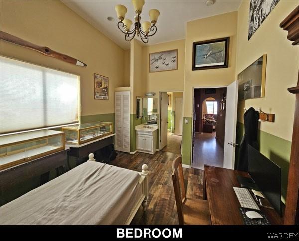 bedroom featuring a towering ceiling, dark wood-style floors, and a notable chandelier