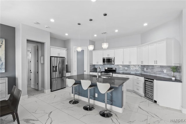 kitchen with stainless steel appliances, wine cooler, decorative light fixtures, and an island with sink