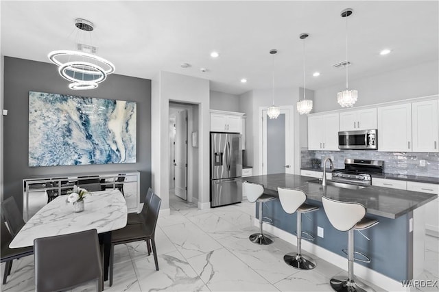 kitchen with hanging light fixtures, appliances with stainless steel finishes, an island with sink, and white cabinets