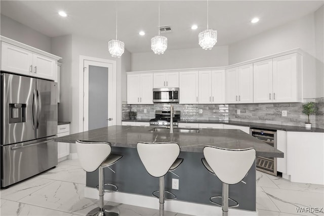 kitchen featuring a kitchen island with sink, beverage cooler, stainless steel appliances, marble finish floor, and pendant lighting