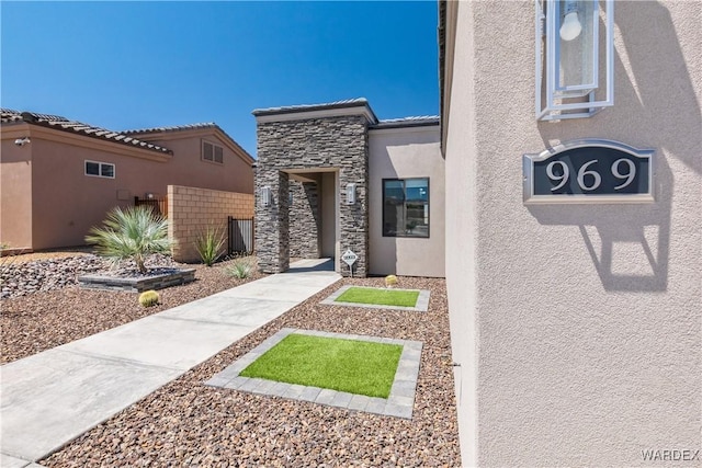 property entrance featuring stone siding, fence, and stucco siding