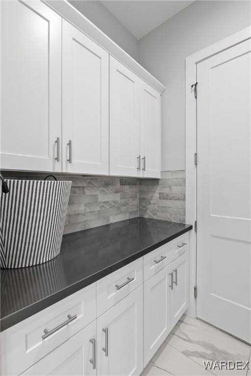 kitchen featuring marble finish floor, dark countertops, backsplash, and white cabinetry