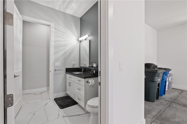 bathroom with toilet, marble finish floor, vanity, and baseboards