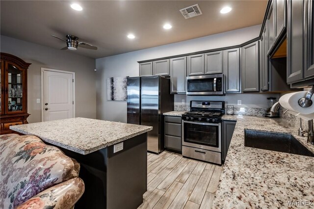 kitchen featuring light stone counters, stainless steel appliances, visible vents, a sink, and ceiling fan