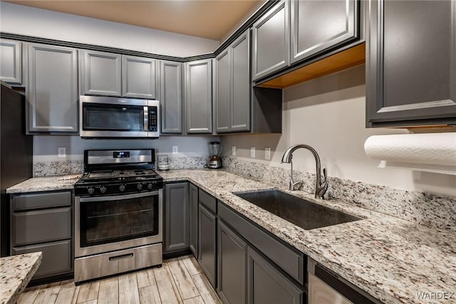 kitchen featuring light stone countertops, a sink, appliances with stainless steel finishes, gray cabinets, and wood tiled floor