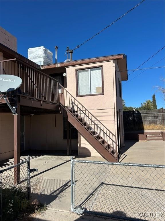 view of property exterior with fence, stairway, and stucco siding