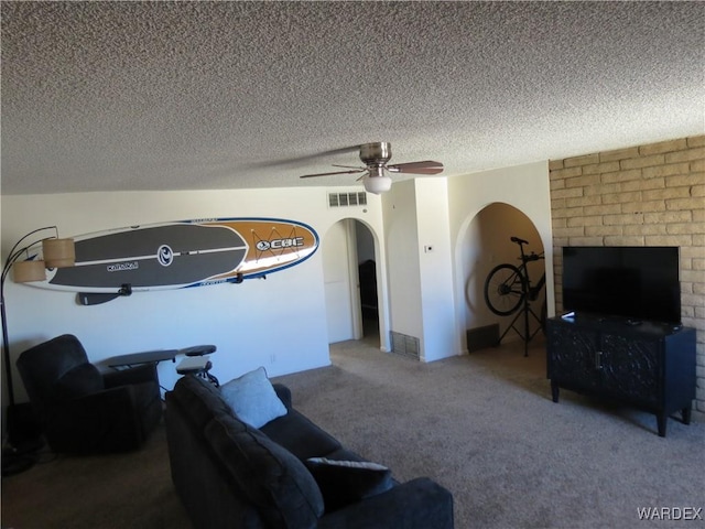 living room featuring arched walkways, a textured ceiling, carpet floors, visible vents, and a ceiling fan