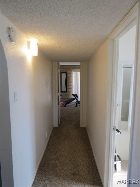 corridor with carpet floors, baseboards, and a textured ceiling