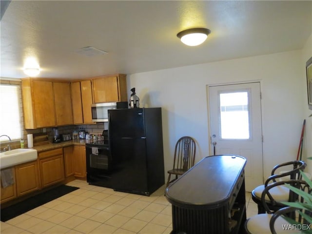 kitchen with light tile patterned floors, tasteful backsplash, brown cabinets, black appliances, and a sink