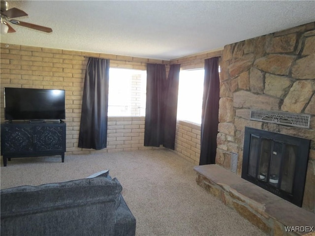 carpeted living room with a ceiling fan, visible vents, a textured ceiling, and a stone fireplace