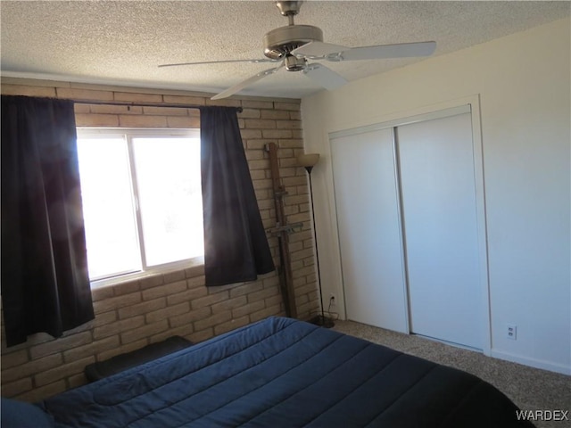 unfurnished bedroom with carpet, a closet, a ceiling fan, a textured ceiling, and brick wall