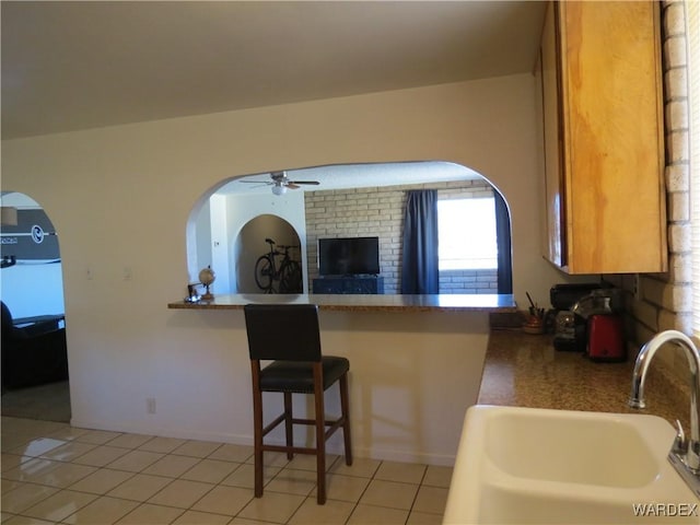 kitchen with light tile patterned floors, ceiling fan, a breakfast bar area, a peninsula, and a sink