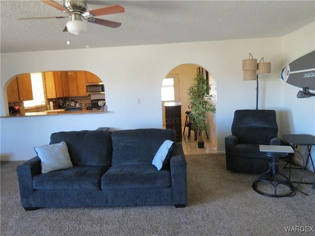 living room with carpet, arched walkways, ceiling fan, and a textured ceiling