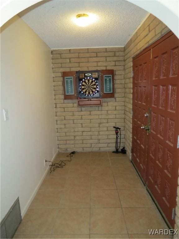 corridor featuring a textured ceiling, tile patterned flooring, brick wall, visible vents, and baseboards