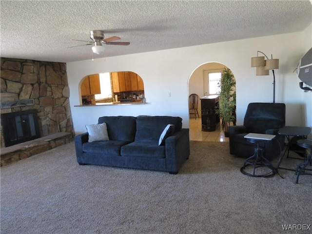 living room featuring arched walkways, a stone fireplace, carpet flooring, and a wealth of natural light