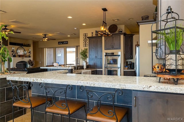 kitchen featuring a breakfast bar area, open floor plan, stainless steel appliances, dark brown cabinets, and a sink