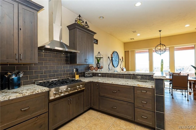 kitchen featuring stainless steel gas cooktop, a peninsula, hanging light fixtures, backsplash, and wall chimney exhaust hood