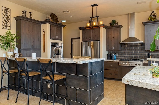 kitchen featuring decorative light fixtures, stainless steel appliances, visible vents, dark brown cabinetry, and wall chimney exhaust hood