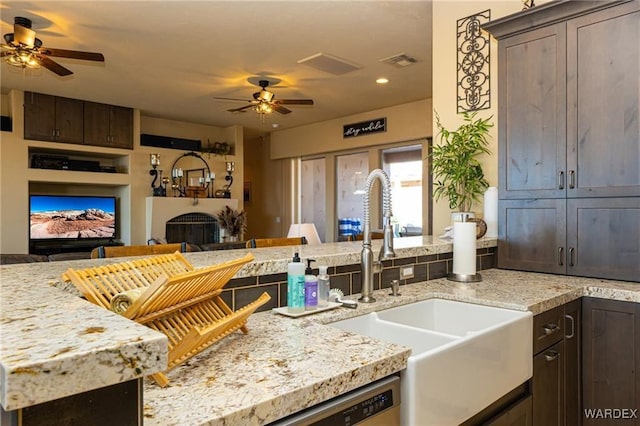 kitchen featuring a fireplace, visible vents, open floor plan, a sink, and dark brown cabinets