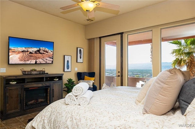 bedroom featuring a water view, visible vents, a ceiling fan, access to outside, and a glass covered fireplace