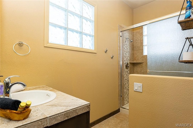 bathroom with tiled shower, vanity, and baseboards