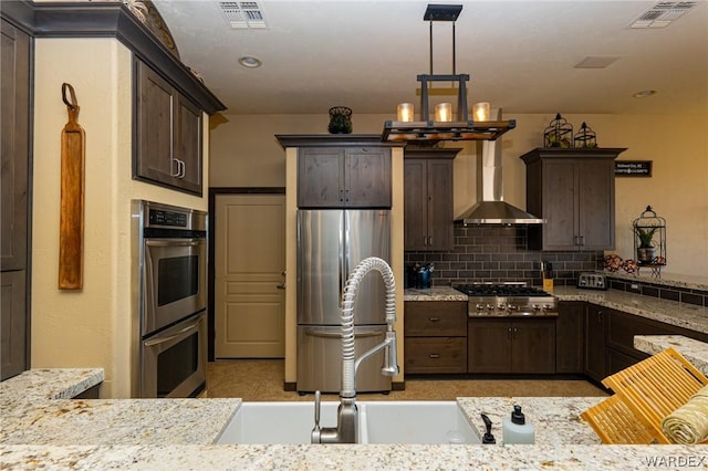 kitchen with wall chimney range hood, appliances with stainless steel finishes, visible vents, and light stone countertops