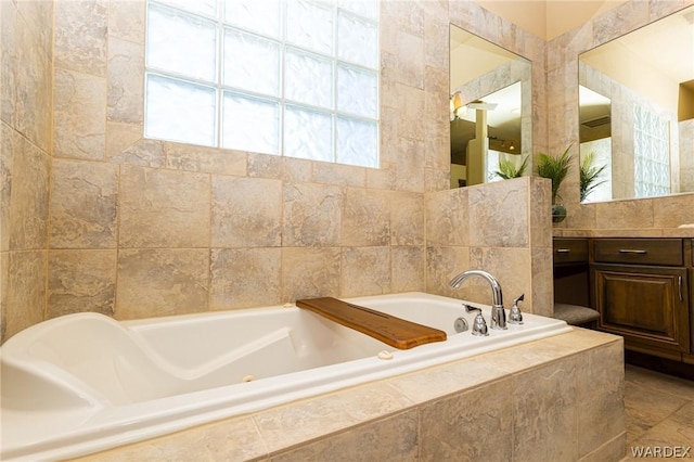 full bath with tile walls, vanity, and a tub with jets