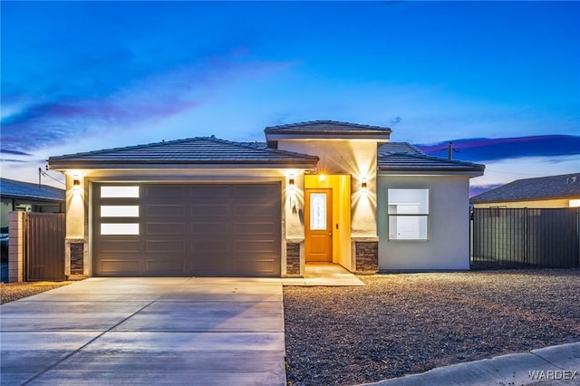 prairie-style house with stucco siding, an attached garage, fence, stone siding, and driveway