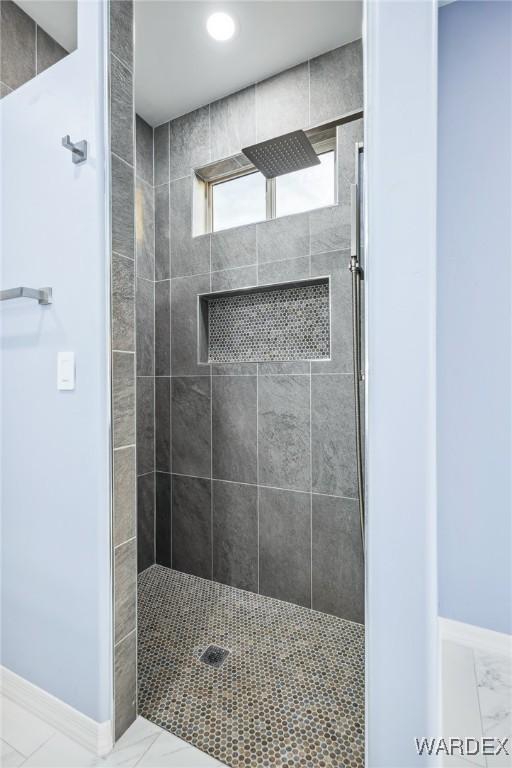 full bath with marble finish floor, baseboards, and walk in shower