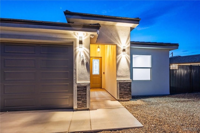 property entrance with a garage, stone siding, fence, and stucco siding