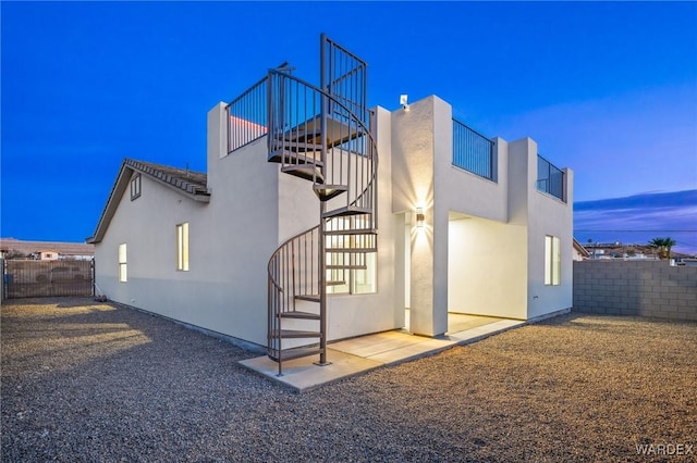 back of property at dusk with fence, stairway, and stucco siding