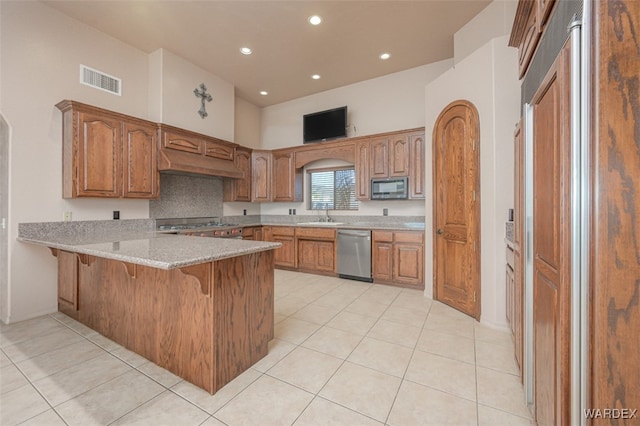 kitchen with a peninsula, stainless steel dishwasher, brown cabinetry, and light stone countertops