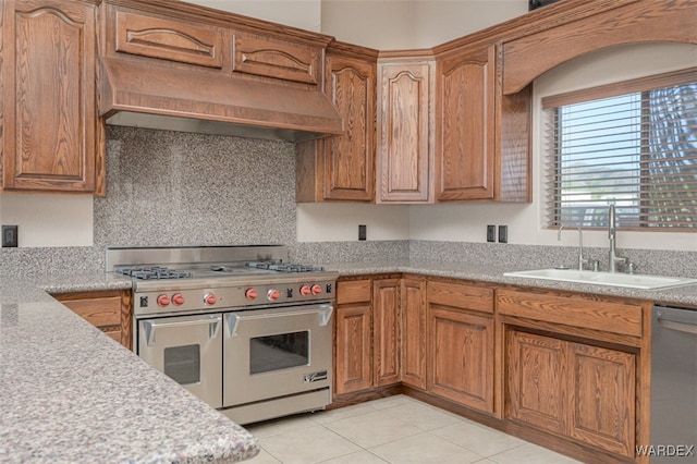 kitchen featuring stainless steel appliances, a sink, light countertops, custom exhaust hood, and brown cabinetry