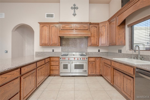 kitchen featuring visible vents, appliances with stainless steel finishes, brown cabinetry, a sink, and ventilation hood