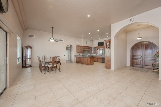 kitchen featuring visible vents, arched walkways, brown cabinets, decorative light fixtures, and light countertops