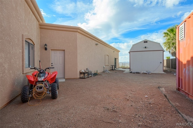 view of property exterior with a storage shed, fence, stucco siding, and an outbuilding