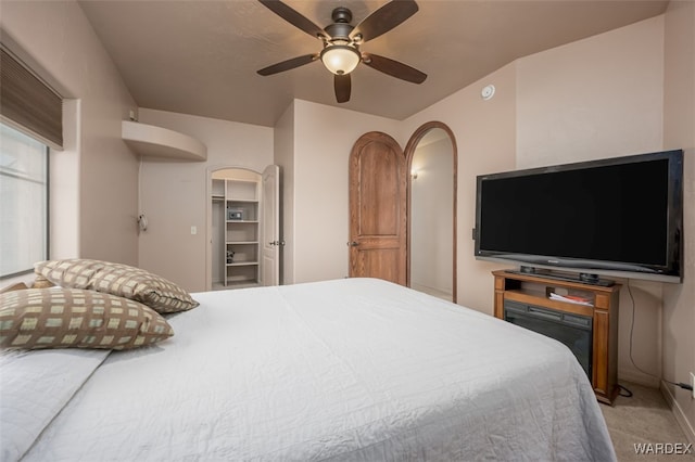 bedroom with light carpet, a spacious closet, arched walkways, and a ceiling fan