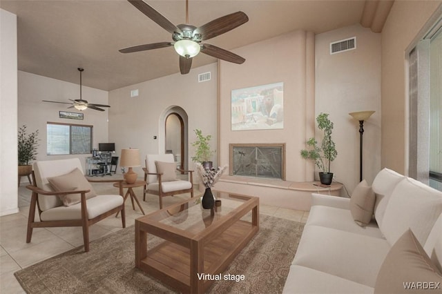 living area featuring light tile patterned floors, visible vents, a fireplace with raised hearth, and arched walkways