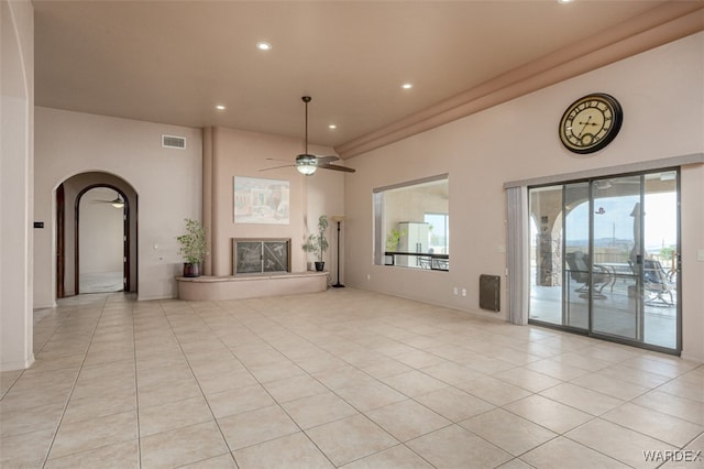 unfurnished living room featuring arched walkways, light tile patterned floors, visible vents, a ceiling fan, and a glass covered fireplace