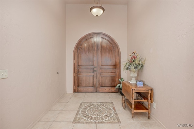 foyer featuring arched walkways, light tile patterned flooring, and baseboards