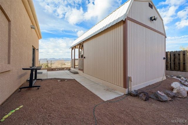 view of property exterior featuring metal roof, a patio area, fence, and a gambrel roof